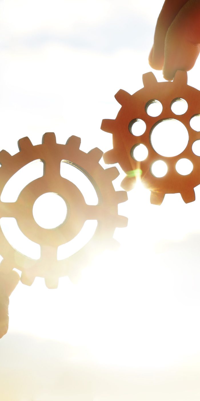 Male hand holding two wooden cog gear wheel on sunny sky background. sunshine and yellow and yellow sky . sun rays.one part of whole. symbol of association and connection. business strategy